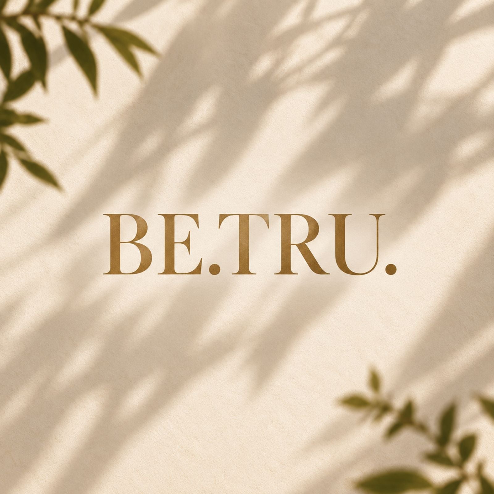 The BE.TRU. wordmark stamped in gold on a wall, dappled with the shadow of leaves